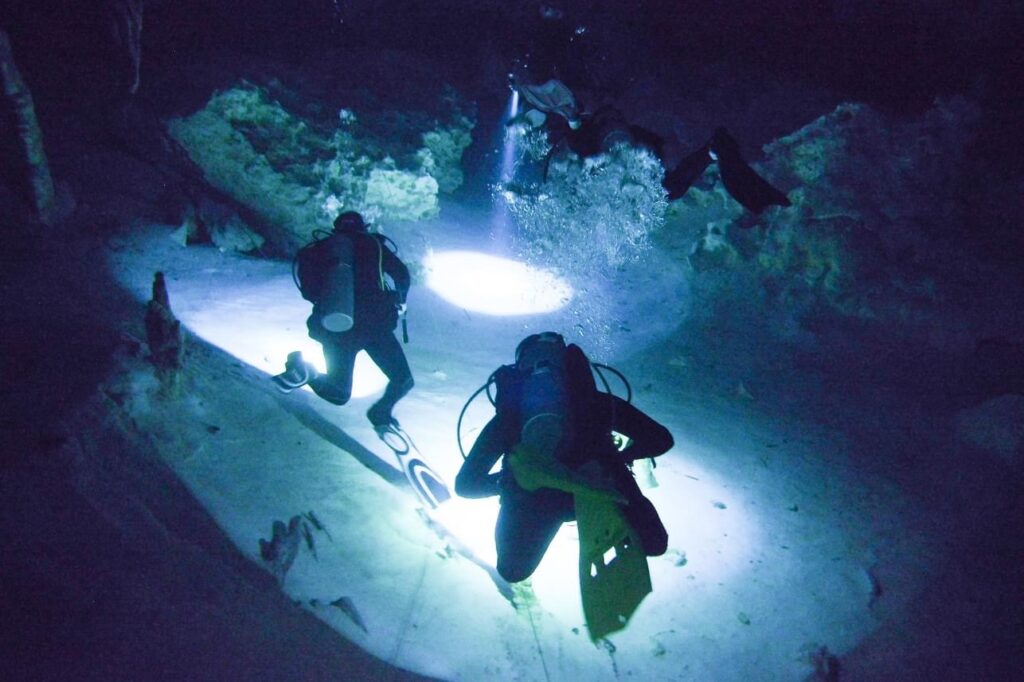 scuba divers in cenote with flashlights